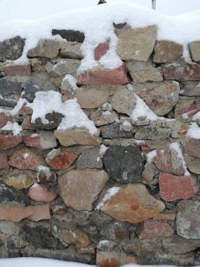 Eski kaya duvar, beton ve grunge dokusu. Antik mimari. Tuğla çit kırmızı, terracotta renginde gri ve siyah taşlardan yapılmış. Duvarda kar var. Kış zamanı  