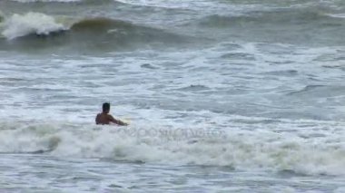 Adam kürekler dışarı Bali bir sahilde fırtınalı bir denizde sörf tahtası