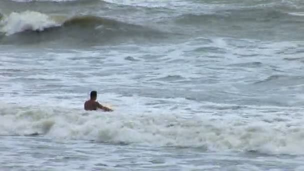 Man paddlar ut på surfbräda i ett stormigt hav på en strand i Bali — Stockvideo