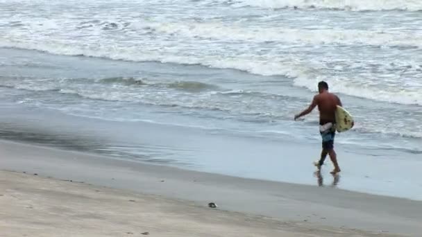 Man paddlar ut på surfbräda i ett stormigt hav på en strand i Bali — Stockvideo