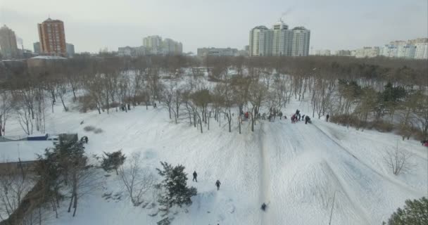 Caméra aérienne vole vers l'arrière à partir d'enfants traînant sur un mont couvert de neige — Video