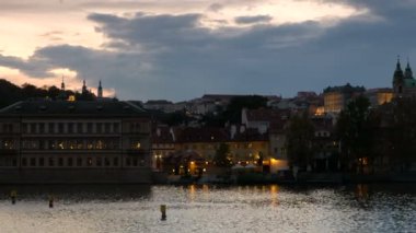 Vltava Nehri Prag Kalesi'ne gece karanlığında pan. Şehrin ışıkları yanıyor. 