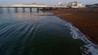 Drone çok yavaş ve düşük Brighton Pier Sussex'te doğru bir puslu yaz şafak küçük dalgalar sonu olarak sırasında kumsalda uçar