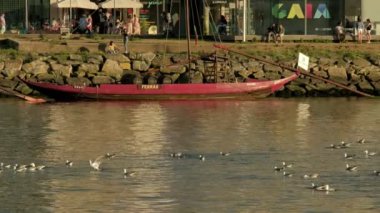 Porto 'daki Douro Nehri' nin kıyısında bir Rabelo teknesinin telefon klibi. Önden büyük bir nehir yolcu gemisi geçiyor.