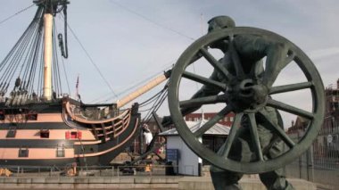 Arka planda HMS Victory olan silah tekerleği taşıyan denizci heykeli. Portsmouth Tarih Tersanesi 'nde çekildi