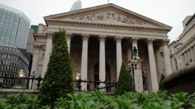 Londra şehrindeki Royal Exchange 'i ortaya çıkarmak için çalıların arkasından kamera yükseliyor. 22 Bishopsgate 'in tepesi bulutların ardında.