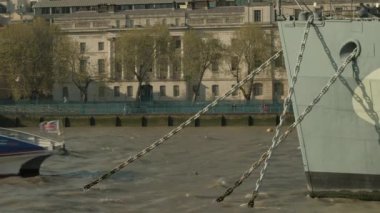 Bir Thames Clipper nehri otobüsü Londra, İngiltere 'de HMS Belfast' ın pruvasının arkasından geçiyor. Güneşli bir günde çekilmiş.