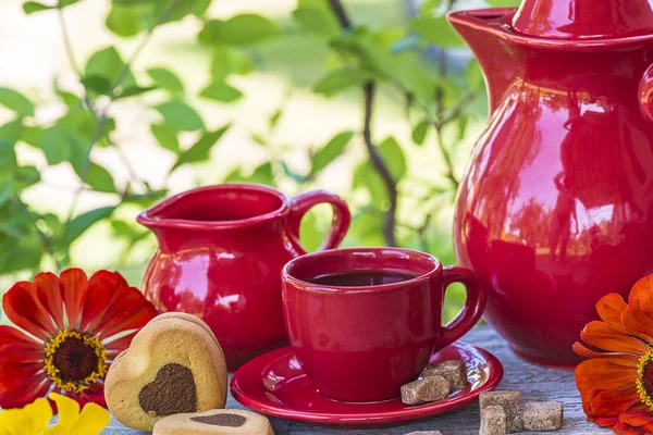 red cup of coffee, red coffee pot, red flowers,cane sugar in the green garden