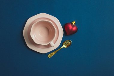 Boş pembe kahve, küçük kaşık ve kırmızı Noel kalbi mavi arka planda fotokopi alanı ile