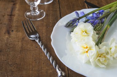 Festive table setting with forged fork and knife and bouquet of daffodils and hyacinths