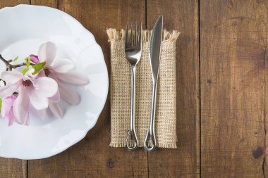 Table setting with magnolia flowers. Forged fork and knife on burlap napkin