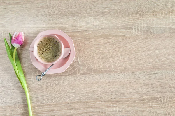 One pink cup of coffee and pink tulip on wooden background. Space for text