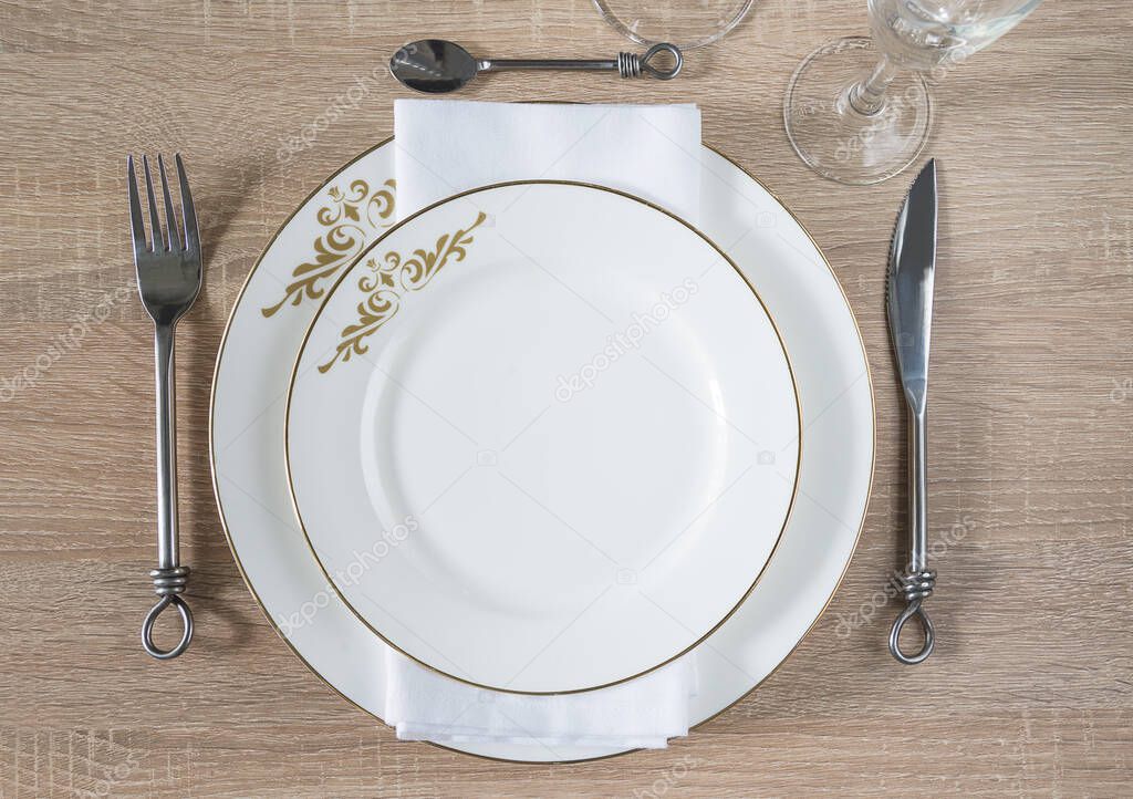 Traditional table setting. Two white plates, napkin, forged knife, fork, spoon, set of wineglasses