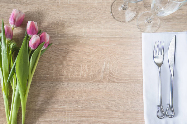 Romantic table setting with bouquet of fresh tulips, forged fork and knife, set of wineglasses