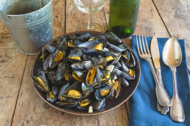 Pişmiş midye tabağı, mavi peçete, şişe ve bir bardak beyaz şarap.