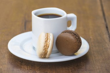 İki Fransız kurabiyesi ve eski ahşap arka planda bir fincan kahve.