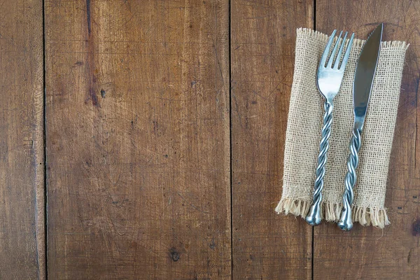 Hand made forged fork and knife on burlap napkin and old wooden background