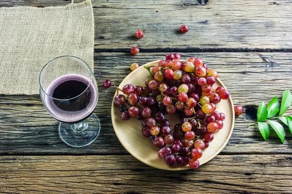 Фиолетовая тарелка винограда, бокал красного вина, положить на старый деревянный стол . — стоковое фото