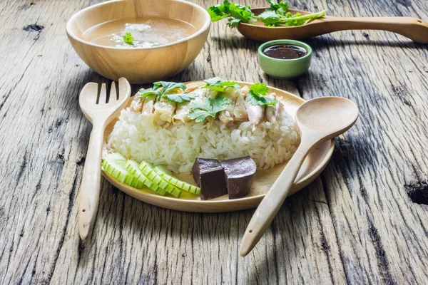 Hainanese tavuklu pilav bir tabakta çorba ve ahşap bir masa sosu ile birlikte. 