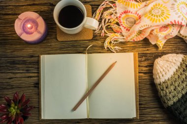 Fincan kahve, defter, mumlar, şapka, eşarp ve eldiven ahşap bir masa üzerinde.