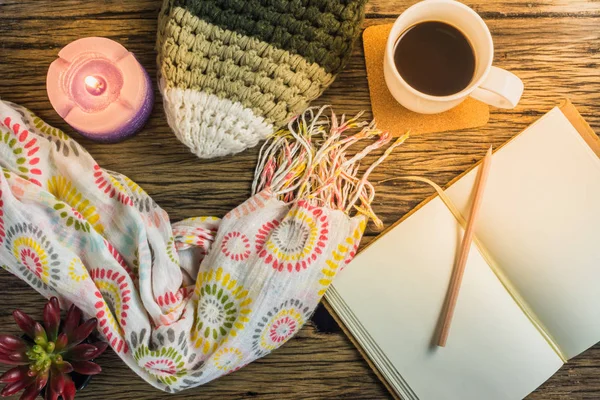 Café, cuaderno, velas, sombreros, bufandas y guantes en una mesa de madera . — Foto de Stock