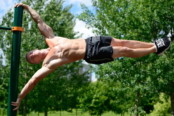 Hombre musculoso practicar entrenamiento callejero en un gimnasio al aire libre — Foto de Stock