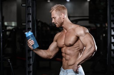 Bir shaker tutarak ve spor salonu fitness ve vücut geliştirme poz yakışıklı atletik fitness adam
