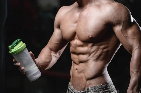 Guapo atlético fitness hombre sosteniendo una coctelera y posando gimnasio — Foto de Stock