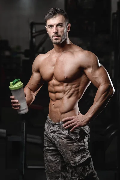 Bel homme de fitness athlétique tenant un shaker et posant gymnase — Photo