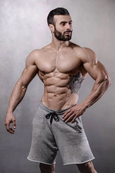 Brutal strong bodybuilder man posing in studio on grey backgroun