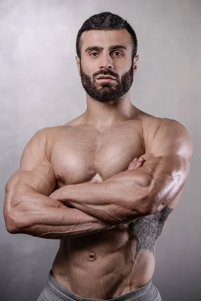 Brutal strong bodybuilder man posing in studio on grey backgroun