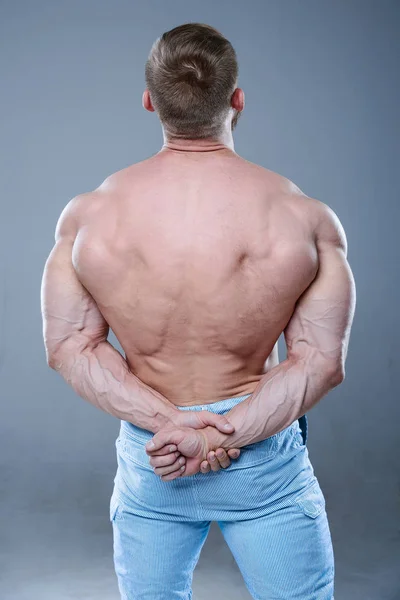 Βάναυση ισχυρή bodybuilder άνθρωπος που θέτουν σε στούντιο στο γκρι backgroun — Φωτογραφία Αρχείου