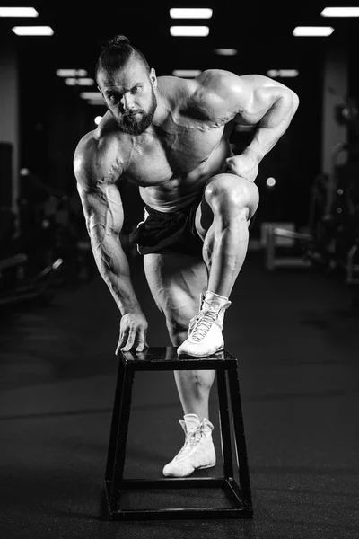 Komea istuvuus valkoihoinen lihaksikas mies taivuttaa lihaksiaan kuntosalilla — kuvapankkivalokuva