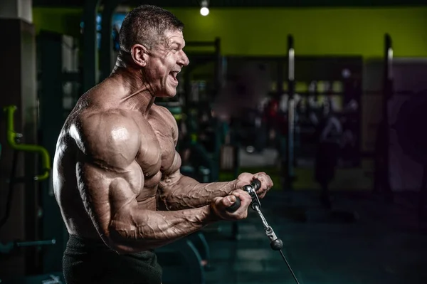 Guapo modelo joven entrenamiento brazos en el gimnasio — Foto de Stock