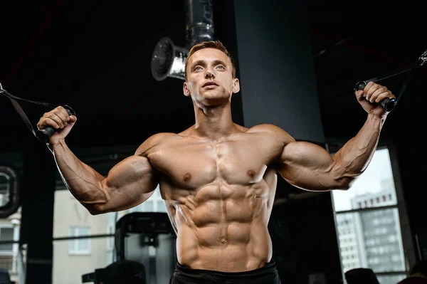 Guapo modelo joven entrenamiento brazos en el gimnasio — Foto de Stock