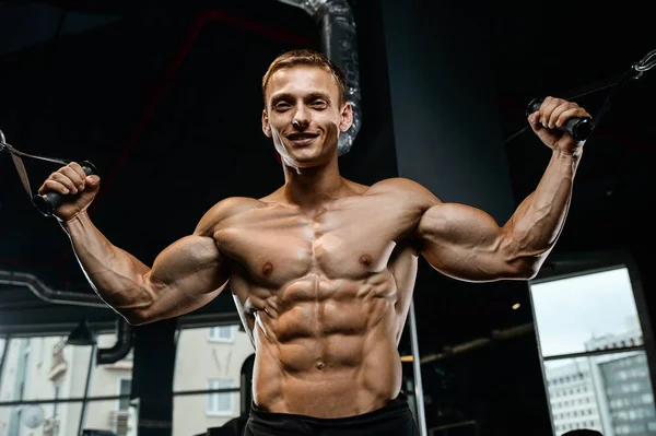 Guapo modelo joven entrenamiento brazos en el gimnasio — Foto de Stock