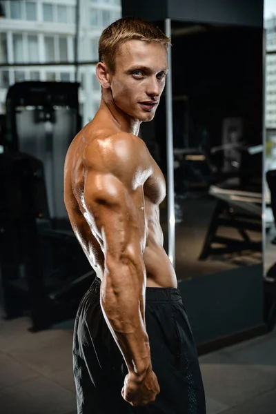 Guapo modelo joven entrenamiento brazos en el gimnasio — Foto de Stock