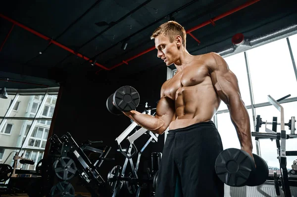 Guapo modelo joven entrenamiento brazos en el gimnasio — Foto de Stock