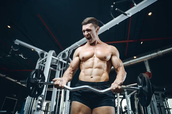 Guapo modelo joven entrenamiento brazos en el gimnasio — Foto de Stock