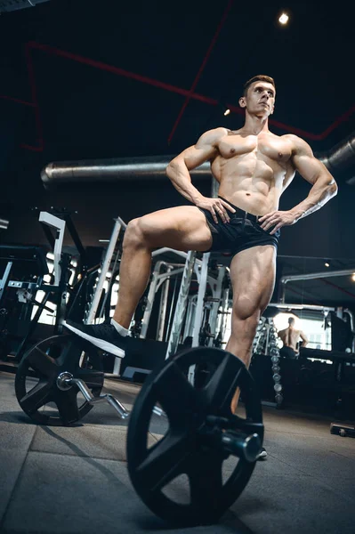 Guapo modelo joven entrenamiento piernas en el gimnasio — Foto de Stock