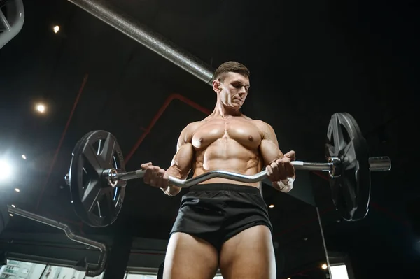 Guapo modelo joven entrenamiento brazos en el gimnasio — Foto de Stock