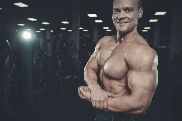 Guapo modelo joven entrenamiento brazos en el gimnasio — Foto de Stock