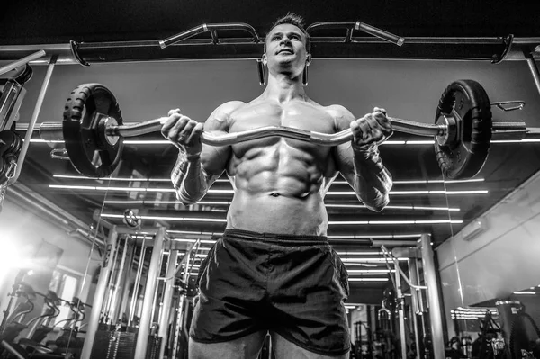 Guapo modelo joven entrenamiento brazos en el gimnasio — Foto de Stock