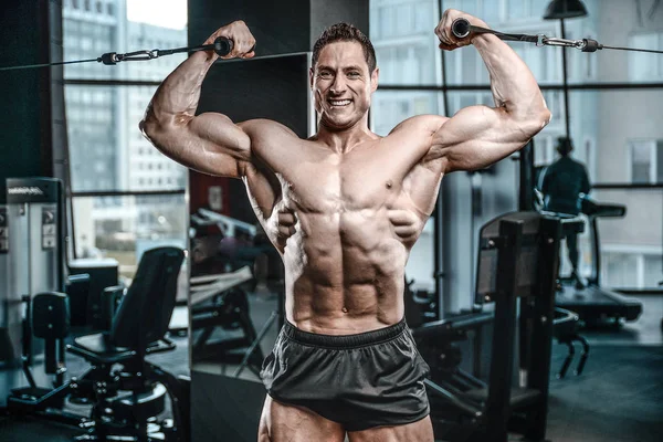 Guapo modelo joven entrenamiento brazos en el gimnasio — Foto de Stock