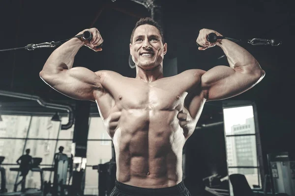 Guapo modelo joven entrenamiento brazos en el gimnasio — Foto de Stock