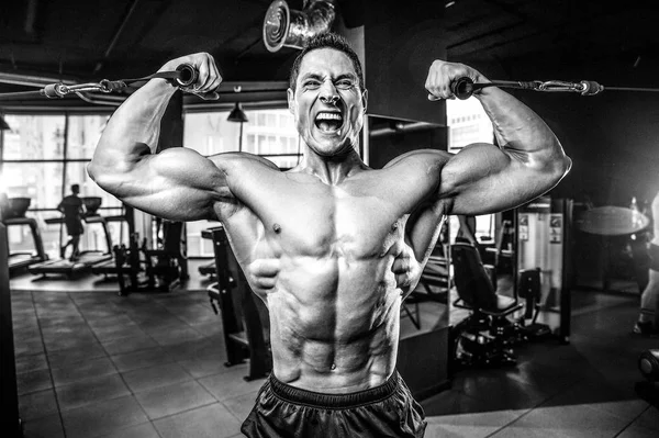 Guapo modelo joven entrenamiento brazos en el gimnasio — Foto de Stock