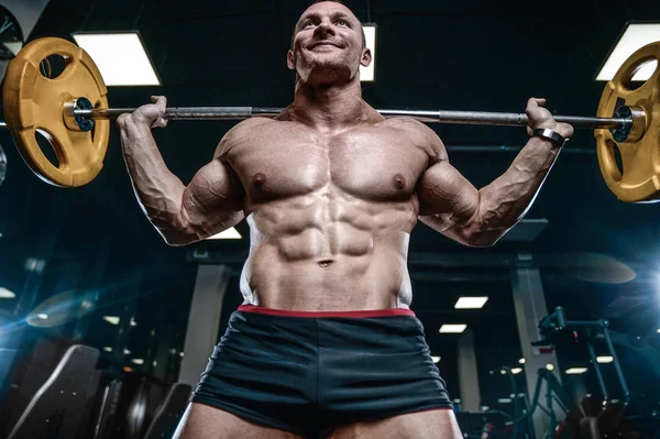 Guapo modelo joven entrenamiento piernas en el gimnasio — Foto de Stock