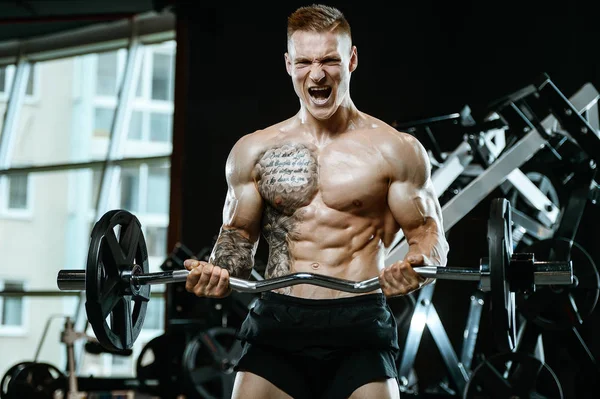 Guapo modelo joven entrenamiento brazos en el gimnasio — Foto de Stock