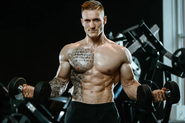 Guapo modelo joven entrenamiento brazos en el gimnasio — Foto de Stock