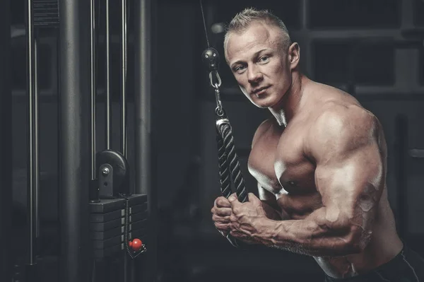 Guapo modelo joven entrenamiento brazos en el gimnasio —  Fotos de Stock